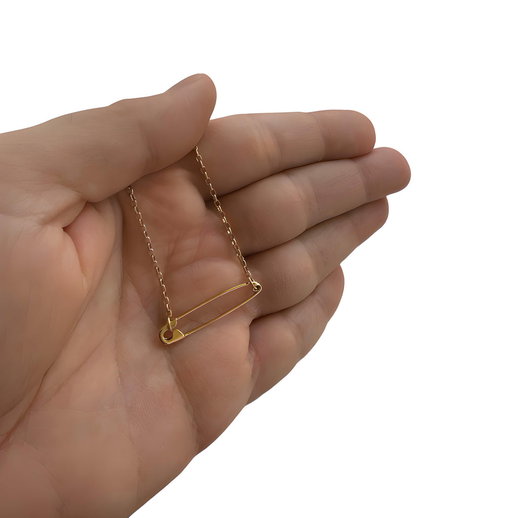 Delicate sterling silver safety pin pendant on a thin chain necklace held in hand.