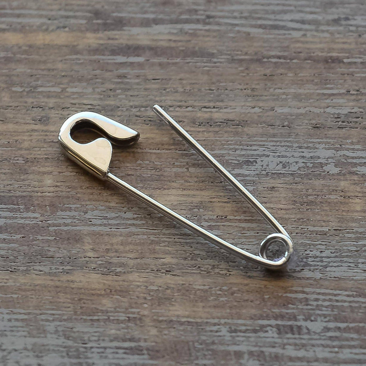 White gold safety pin earring with sleek, polished finish on wooden surface.