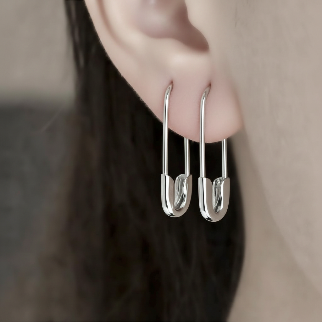 Minimalist silver-tone safety pin hoop earrings on ear, 3/4 inch length, sleek modern design worn on earlobe .